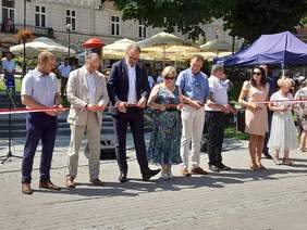 Słoneczny dzień, na przemyskim rynku grupa osób przecina wstęgę