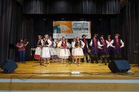 Występ kilkunastu osób mężczyzn i kobiet w strojach ludowych