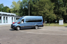 Pokaż zdjęcie: Zdjęcie boku granatowego busa z kokardą na masce.