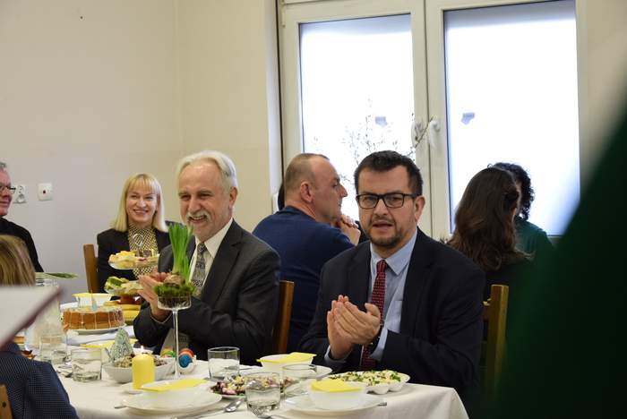 Pokaż zdjęcie: Dyrektor Oddziału PFRON obok osób z niepełnosprawnościami, przy świątecznym stole, ubrany w garnitur