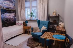 Pokaż zdjęcie: Widok na pokój wyposażony w łóżko, szafkę nocną, fotel, stół i komodę. Nad łóżkiem fototapeta z widokiem na staw.