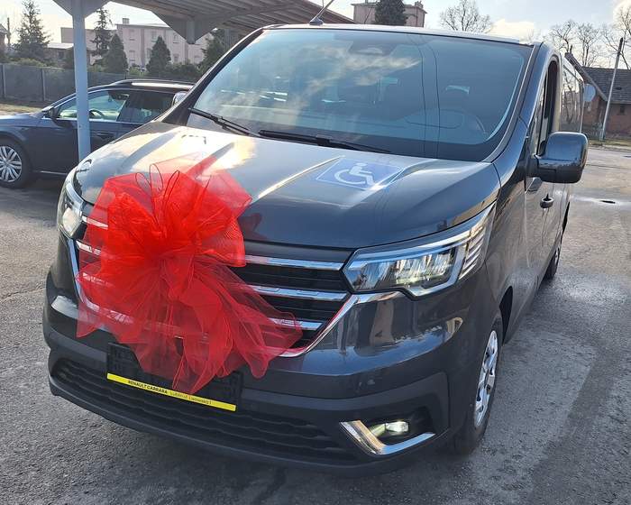 Pokaż zdjęcie: Bus w ciemnym kolorze owinięty czerwoną kokardą na masce