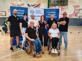 Pokaż zdjęcie: W hali sportowej pozują do zdjęcia przedstawiciele Fundacji Aktywnej Rehabilitacji z regionu łódzkiego. Wszyscy są ubrani w firmowe koszulki. 