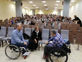 Uczestnicy spotkanai siedzą w auli i czekają na rozpoczęcie. Na pierwszym planie Dyrektor Kujawsko-Pomorskiego Oddziału PFRON rozmawia z dwoma prelegentami - panami na wózkach inwalidzkich.