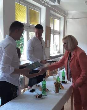 Pokaż zdjęcie: Dyrektor Marta Mordarska wita się z dziewczynką, podaje jej rękę. Obok dziewczynki stoją dwaj mężczyźni. Wszyscy się uśmiechają.