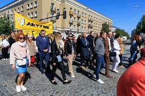 Pokaż zdjęcie: Po brukowanej ulicy idą ludzie niosą żółte banery z jeden z nich z napisem Aktywni 