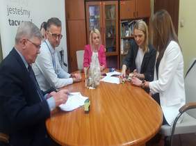 Pokaż zdjęcie: na zdjęciu pomieszczenie w Oddziale, duży stół owalnym przy którym siedzi 5 osób, podpisują dokumenty związane z dofinansowaniem PFRON 