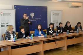 Pokaż zdjęcie: Prelegenci konferencji: wicewojewoda wielkopolski Aneta Niestrawska, prezes Zarządu PFRON Marlena Maląg, dyrektor oddziału wielkopolskiego PFRON Anna Skupień, a także przedstawiciele organizacji pozarządowych z Wielkopolski siedzą za stołem konferencyjnym