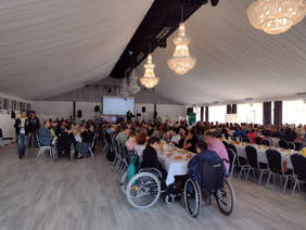 na sali trzy rzedy stołów przy których siedzą zebrani goście w tym osoby na wózkach inwalidzkich