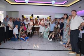 Pokaż zdjęcie: Na tle tortu pozuje do pamiątkowego zdjęcia duża grupa osób, uczestników Warsztatu Terapii Zajęciowej.