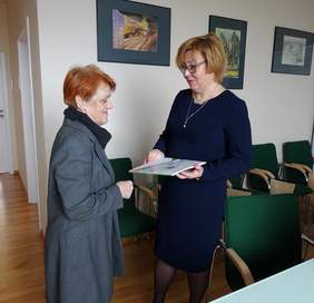 Pokaż zdjęcie: Helena Maślana – prezes Fundacji Sztuki Osób Niepełnosprawnych oraz Marta Mordarska - dyrektor Oddziału Małopolskiego PFRON na tle prac osób niepełnosprawnych, które Fundacja przekazała dla Oddziału 