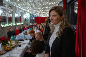 Pokaż zdjęcie: Zdjęcie długiego stołu przy którym siedzą zaproszeni goście. Stół jest udekorowany świątecznie.