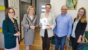 Pokaż zdjęcie: Cztery kobiety i jeden mężczyzna. Wszyscy stoją w sali konferencyjnej, w rękach trzymają teczki z dokumentami