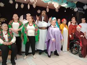 Pokaż zdjęcie: Pensjonariusze Domu Pomocy Społecznej w Dąbrowie śpiewają kolędy i pastorałki. Mają na sobie przebrania kolędników.   