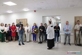 Pokaż zdjęcie: Na korytarzu w ośrodku duża grupa osób stoi przy ścianie, na środku ksiądz święci pomieszczenia ŚDS