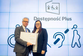 Pokaż zdjęcie: dwie osoby na tle napisu Dostępność Plus