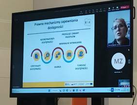 Pokaż zdjęcie: na zdjęciu duży telebim na którym jest prezentacja którą omawia osoba on-line