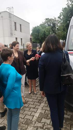 Pokaż zdjęcie: Uroczyste przekazanie kluczyków do autobusu dla WTZ w Chełmie – uczestnicy wydarzenia stoją obok nowego pojazdu, jedna z osób przekazuje kluczyki, w tle budynek placówki.