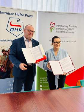 Pokaż zdjęcie: Przedstawiciele Lubelskiej Wojewódzkiej Komendy OHP i Oddziału Lubelskiego PFRON prezentują podpisane porozumienie o współpracy na tle banerów obu instytucji.