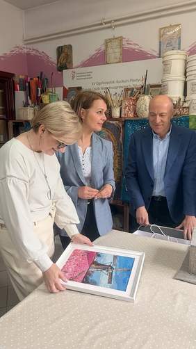 Pokaż zdjęcie: Edyta Kondzior, Dyrektor Podlaskiego Oddziału PFRON, wraz z pracownikami ogląda pracę plastyczną w pracowni artystycznej.