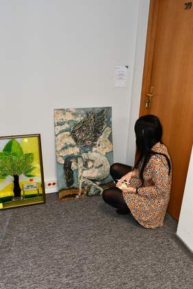 Pani Dorota Jankowska, kucając, przygląda sie jednej z prac.