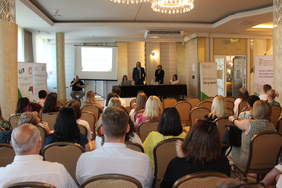 Pokaż zdjęcie: W sali konferencyjnej za stołem prezydialnym siedzą cztery osoby, trzy kobiety i jeden mężczyzna, po lewej stronie ekran z prezentacją