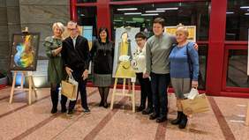 Pokaż zdjęcie: Poseł Urszula Rusecka wraz z Laureatami konkursu Sztuka Osób Niepełnosprawnych. Wszyscy stoją obok prac plastycznych nagrodzonych w konkursie. Prace ustawione są na wysokich, drewnianych sztalugach