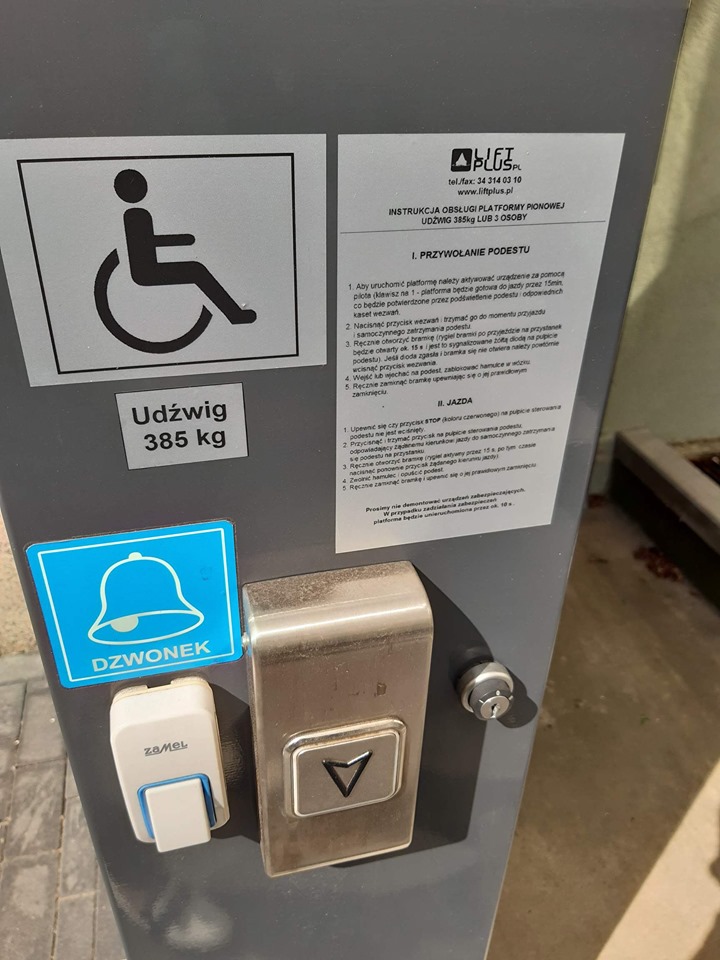 Panel sterowniczy platformy. Panel sterowniczy platformy; na szarym tle umieszczone informacje - jasnoszara plakietka z piktogramem osoby na wózku inwalidzkim, a pod nią plakietka z napisem udźwig 385 kilo. Po prawej stronie od tego piktogramu instrukcja obsługi platformy z opisem jak przywołać podest i kiedy następuje jazda. Poniżej mamy na niebieskim tle piktogram oraz napis dzwonek, pod którym znajduje się przycisk dzwonka. Na prawo od dzwonka duży przycisk do przywołania platformy na poziom zero oraz zamek służący do otwierania i zamykania panelu