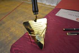 Na stole przykrytym złotym obrusem stoi złota łopatka, która ma być użyta do wmurowania aktu erekcyjnego budowy SOSW w Bystrzycy. Na stole leżą również dwa długopisy
