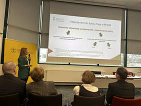 Pokaż zdjęcie: stojąca kobieta w Sali konferencyjnej, na ekranie wyświetla się prezentacja